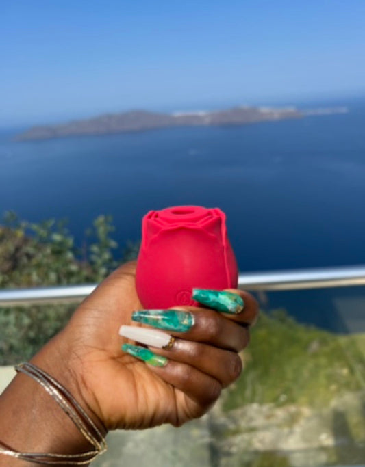 a dark skinned hand holding the rose toy in front of a seaside balcony